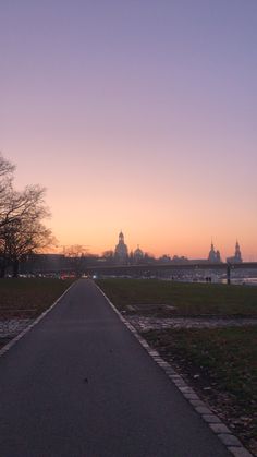 the sun is setting on an empty road in front of a large body of water