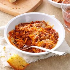 a white bowl filled with pasta and meat on top of a table next to bread