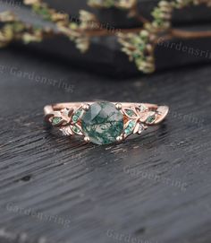 a ring with green stones and leaves on it sitting on a table next to flowers