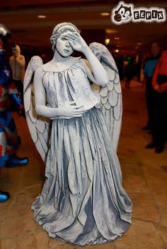 a statue of an angel holding her hands to her face with other people in the background