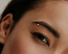 a close up of a woman's face with gold nose piercings on her forehead