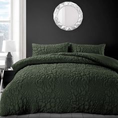 a bed with green comforter and pillows in front of a round mirror on the wall