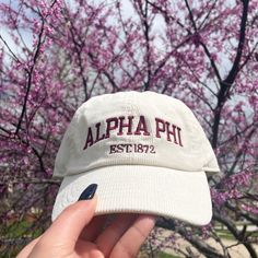 a person holding up a white hat with the word, alpha phi on it