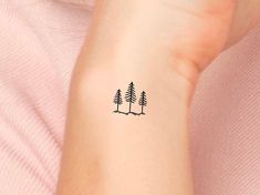 a small pine tree tattoo on the left inner arm and wrist, with trees in the background