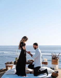 a man kneeling down next to a woman on top of a snow covered ground near the ocean