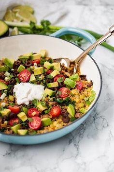 a bowl filled with rice and vegetables on top of a table next to sliced avocado