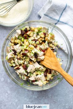 a glass bowl filled with chicken salad next to a wooden spoon