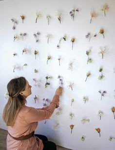 a woman arranging flowers on a wall in front of a white board with lots of them