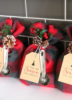 three red and black plaid bags with christmas decorations on them, each bag has a label that says tis the season