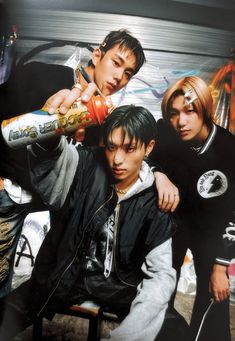 three young men standing next to each other in front of a wall with graffiti on it