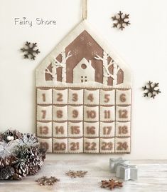 a cross stitch calendar hanging on the wall next to some pine cones and snowflakes