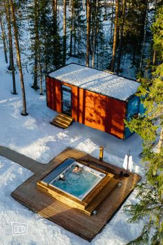 an aerial view of a hot tub in the snow with trees and a cabin behind it