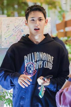 the young man is wearing a blue hoodie and looking at his cell phone while standing in front of him