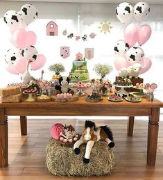 a table topped with lots of balloons and farm animals on top of hay bales