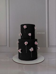 three tiered black cake with pink flowers on it