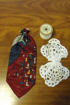 a red tie and some crochet doily on a wooden table next to a spool of thread