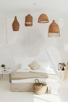 a bedroom with white walls, wicker lamps and a surfboard on the bed