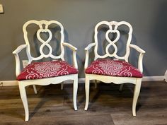 two white chairs with red cushions in front of a gray wall and wood flooring