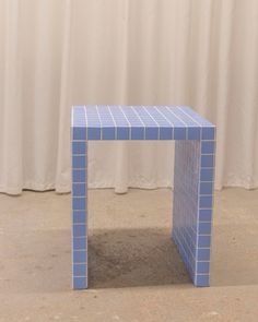 a small blue table sitting on top of a floor next to a white drapes