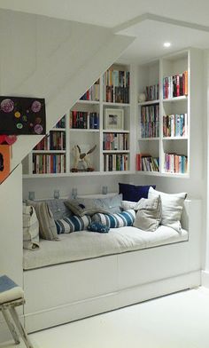 a living room filled with lots of furniture and bookshelves next to a stair case