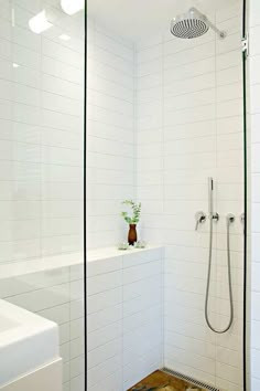 a white tiled bathroom with a shower head and standup shower in the corner next to a sink