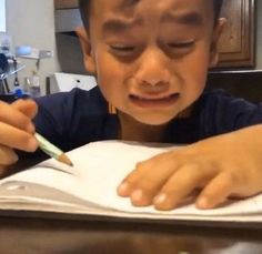 a little boy that is sitting at a table with a pen in his hand and writing on paper