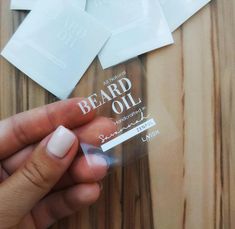 someone is holding up a package of beard oil on a wooden table with other items