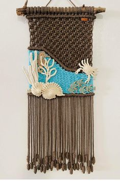 a woven wall hanging with shells and seaweeds on blue, brown and white fabric