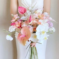 a bride holding a bouquet of flowers in her hands and wearing a white dress with pink accents