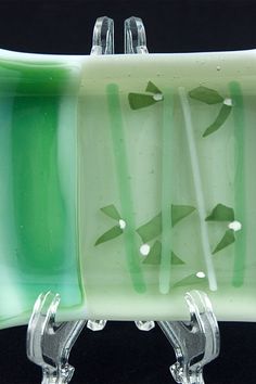 a green and white glass dish sitting on top of a metal stand with two forks sticking out of it