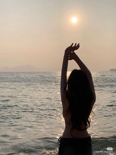 a woman is standing in the water with her arms up to the sun above her head