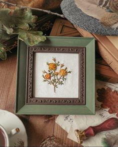 cross stitch flowers in a frame sitting on a table next to other items and leaves