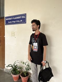 a man standing in front of a building with plants and a bag on his shoulder