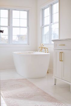 a white bath tub sitting in a bathroom next to two windows and a rug on the floor