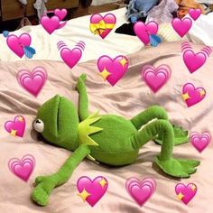 a green stuffed animal laying on top of a bed covered in pink heart shaped hearts