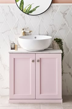 a white sink sitting under a mirror next to a pink cabinet