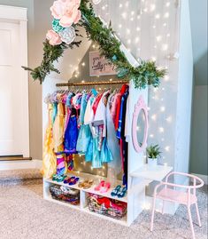 a closet filled with lots of clothes next to a pink chair and white wall covered in lights