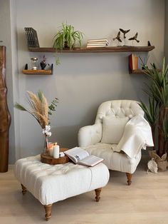 a white chair and ottoman in a room with books on shelves above them, plants are sitting on the shelf