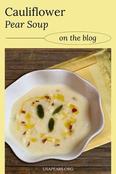 a white bowl filled with soup sitting on top of a wooden table next to a napkin