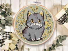 a cross stitch pattern with a grey cat sitting in front of some greenery and presents