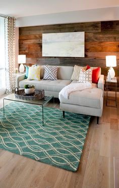 a living room filled with furniture and pillows on top of a blue rug in front of a wooden wall