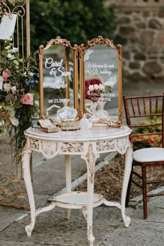 two mirrors sitting on top of a table next to chairs and flowers in vases