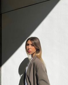 a woman standing in front of a white wall with her hand on her hip and looking off to the side