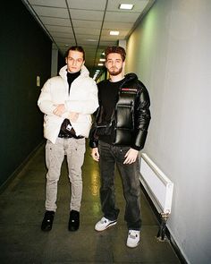 two men standing next to each other in a hallway