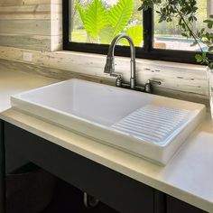 a white sink sitting under a window next to a vase with flowers in front of it