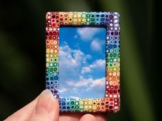 a hand holding up a small photo frame with a sky and clouds in the background