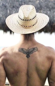 the back of a man with a hat on his head and a bird tattoo on his chest