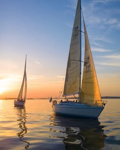 two sailboats in the water at sunset