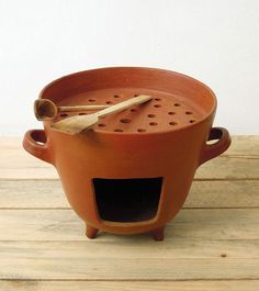 a clay pot with a wooden spoon in it on top of a wood table next to a white wall