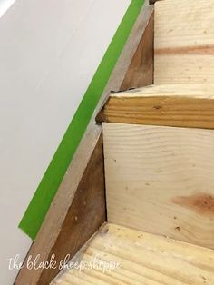 the bottom part of a wooden staircase with green tape on it and white wall in background